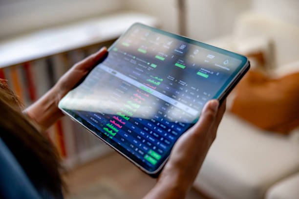 Woman using a stock market app on a tablet at home for financial planning.