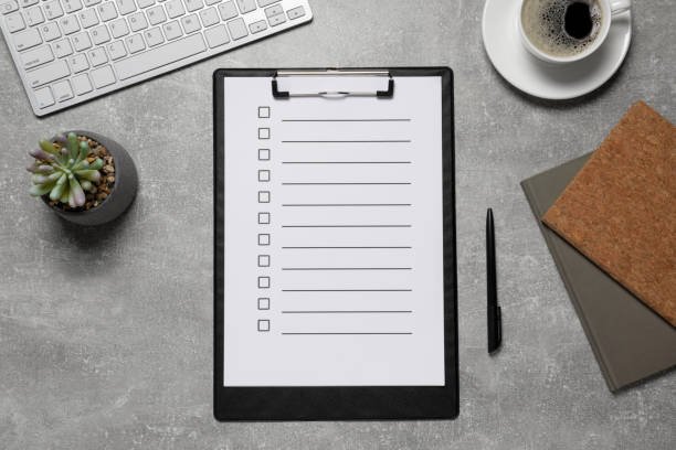Clipboard with checklist, cup of coffee, potted plant, and computer keyboard on a gray workspace — flat lay view