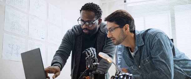 Two male developers coding a robotic arm using a computer.