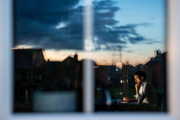 Stressed businessman working late on his laptop at home, sunset light in the background.