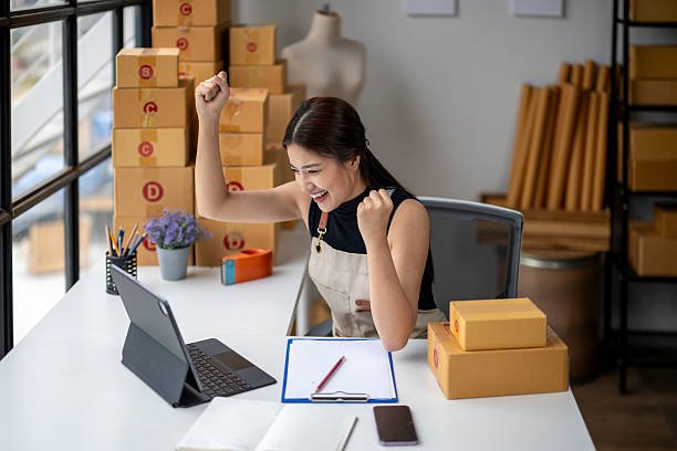 Successful Asian female online seller smiling and celebrating business growth while working on a tablet in her office.