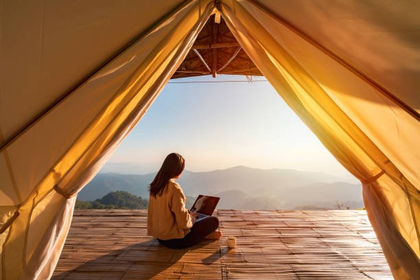 Young woman freelancer working online on a laptop while enjoying a mountain landscape at sunrise