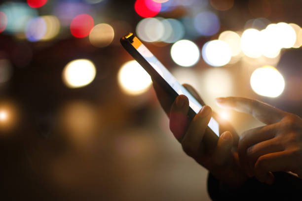 Close-up of female hands using a mobile smartphone with colorful light bokeh on a street at night.